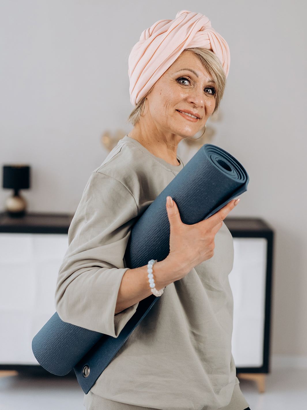 Smiling senior woman holding rolled yoga mat under her arm